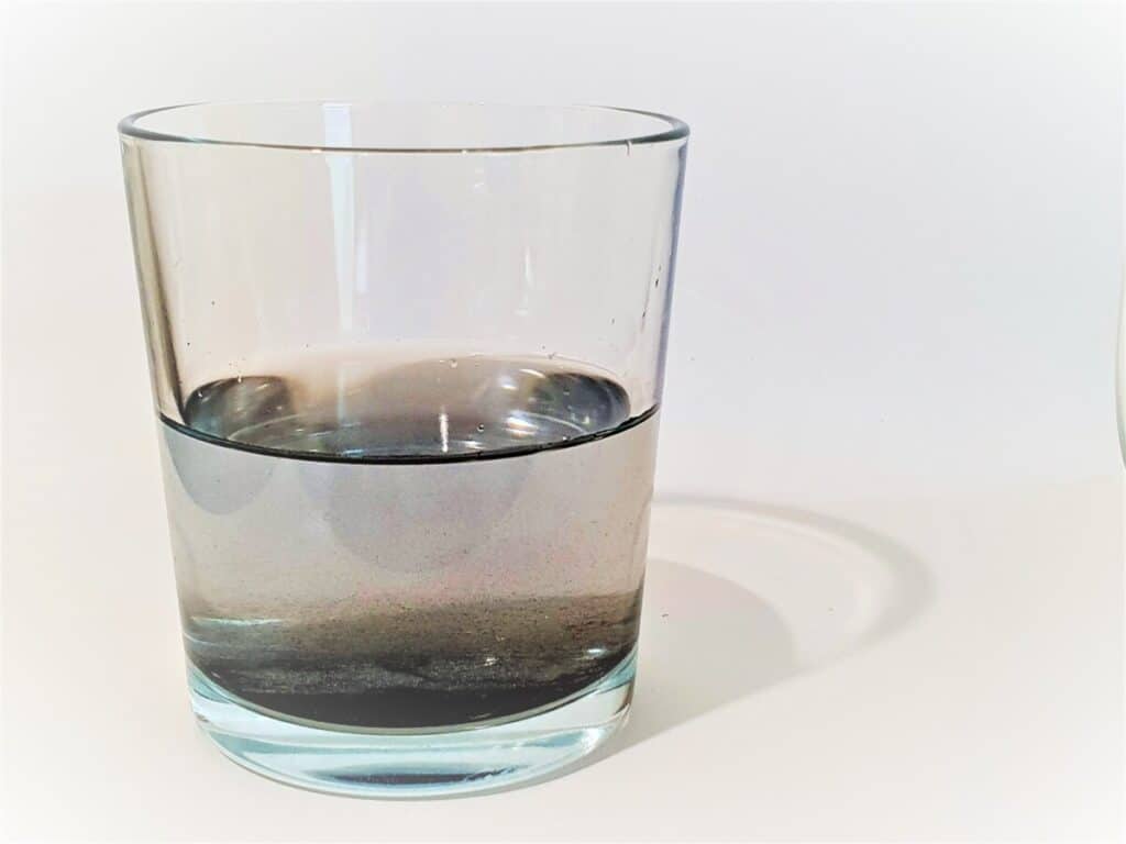 Glass of water containing black particles.